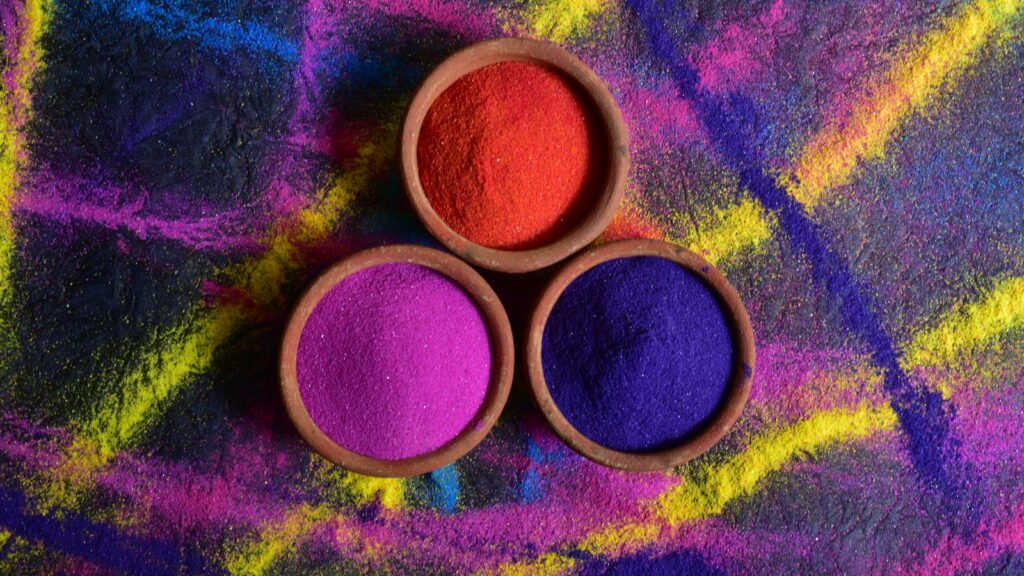 Bowls holding mounds of loose red, blue and purple powder against a brightly coloured background