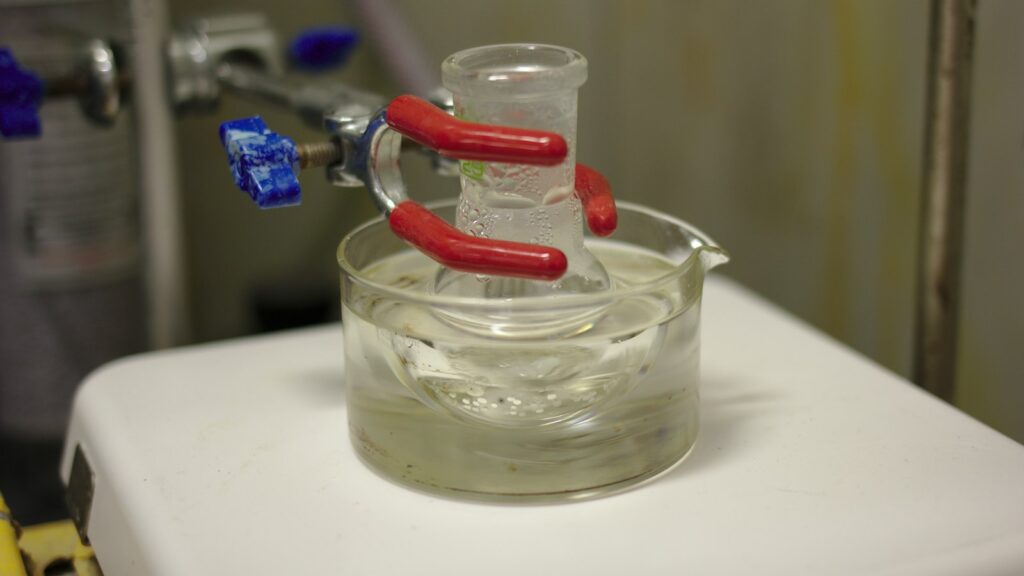 Close-up of a glass reaction vessel being stirred and heated in an oil bath in a chemistry laboratory