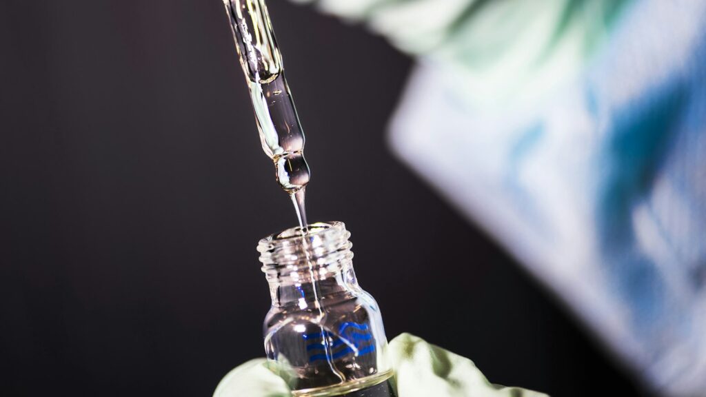 CJC-1295 vs Ipamorelin: How the Two Peptides Differ 1 Gloved hand dripping liquid from a glass pipette into a vial in a research laboratory