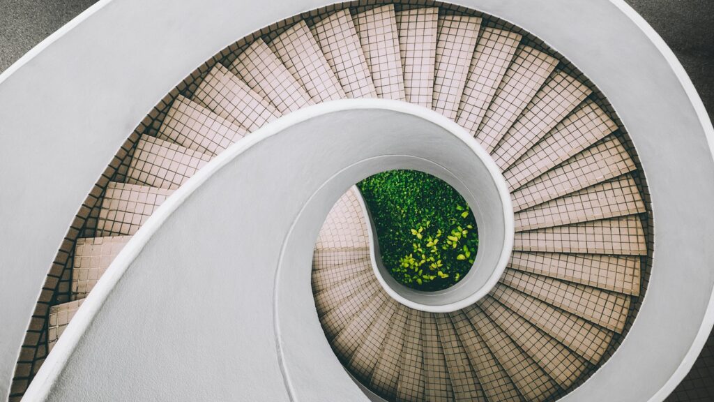 Clinical Trial Phases Explained: From Phase 0 to Phase IV 1 Looking down a white spiral staircase that coils around a small planted garden at its base