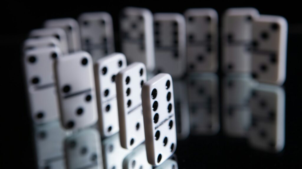 A line of white dominoes with black dots standing in a curve on a dark reflective surface