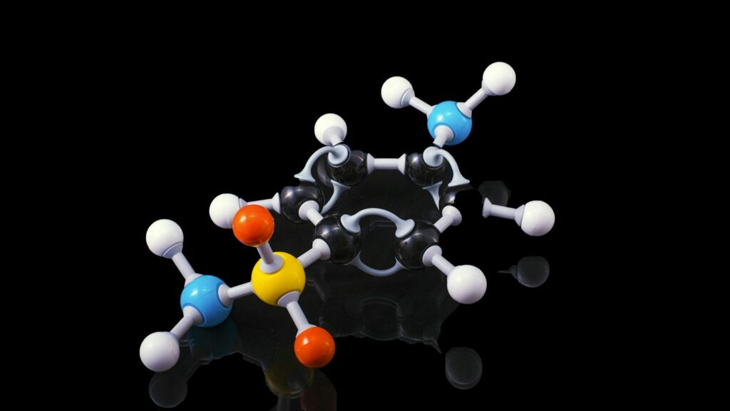Dipeptides, Tripeptides and Oligopeptides: Short Peptides Explained 1 Ball-and-stick molecular model with coloured spheres on a dark reflective surface