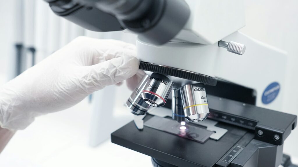 Researcher in white gloves looking through a laboratory microscope