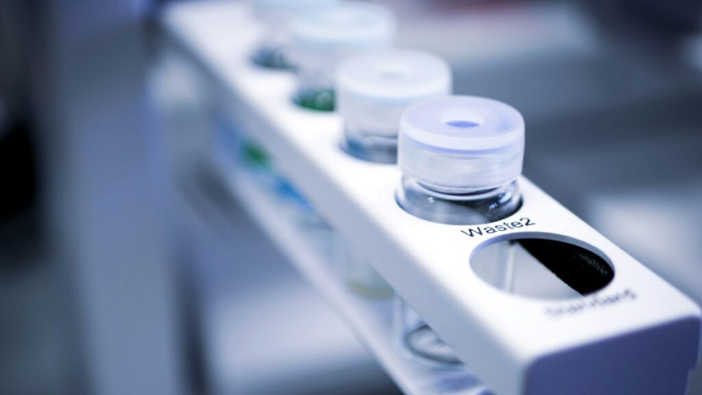 Small glass vials seated in a white rack on a laboratory instrument, in cool blue light