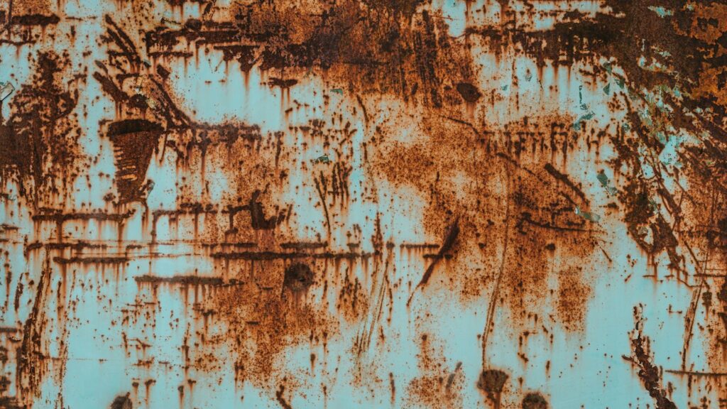Orange rust spreading across a scratched, turquoise-painted metal surface