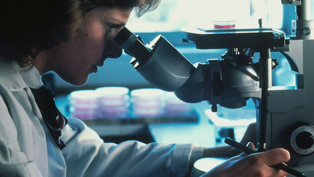 Scientist in a white lab coat looking through a microscope, illustrating thymosin alpha-1 immunology research